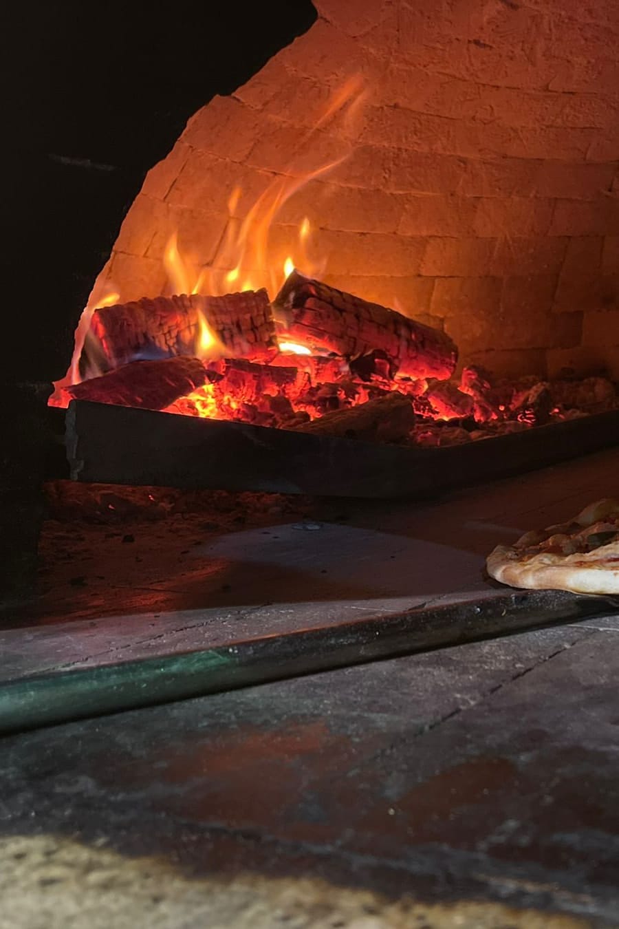 Donna Ginas vedugn med glödande ved och en nybakad pizza på spaden
